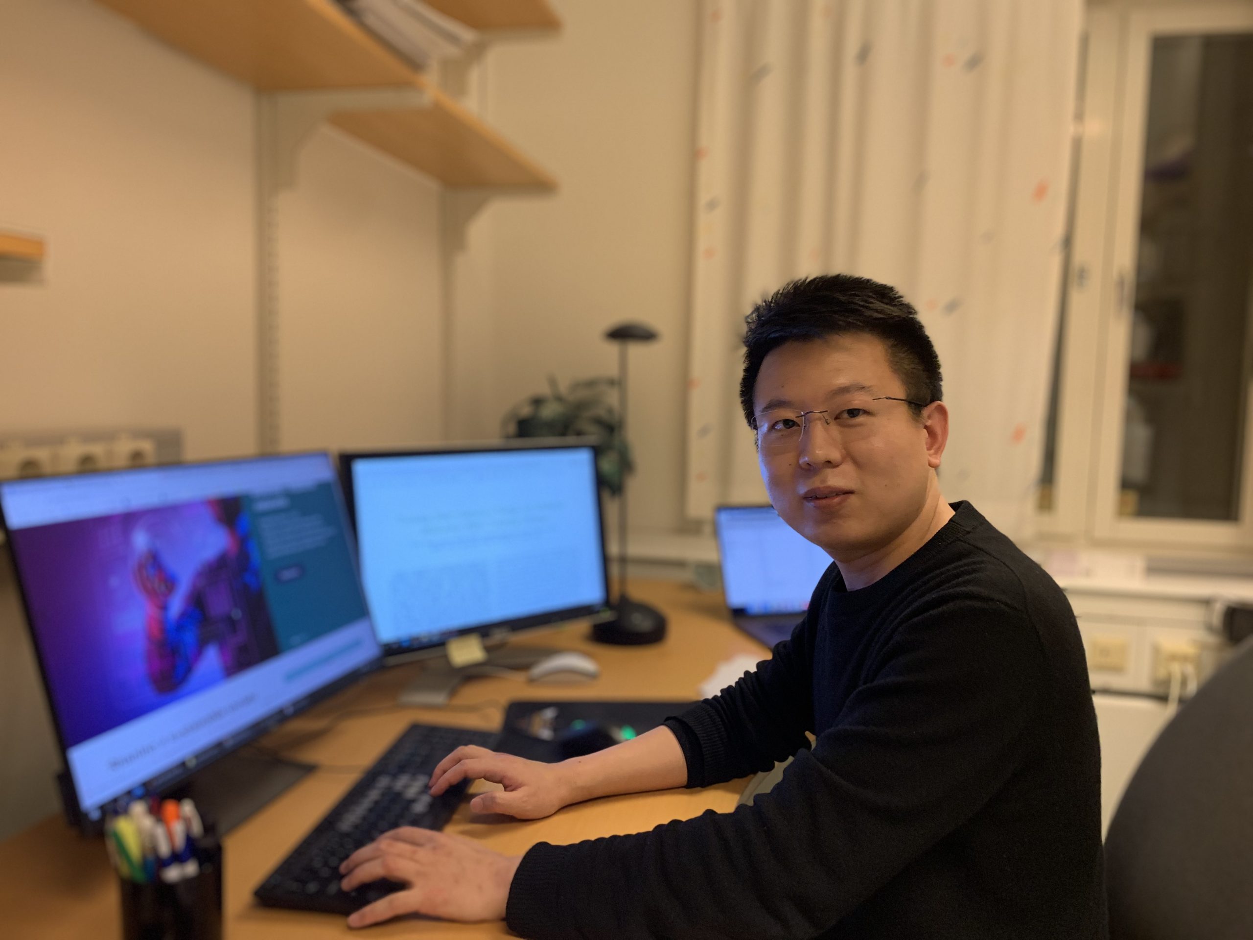 Picture of Deyou Zhang at a desk with computer screens